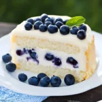 Zitronen-Blaubeer-Kuchen auf einem Teller, dekoriert mit frischen Blaubeeren